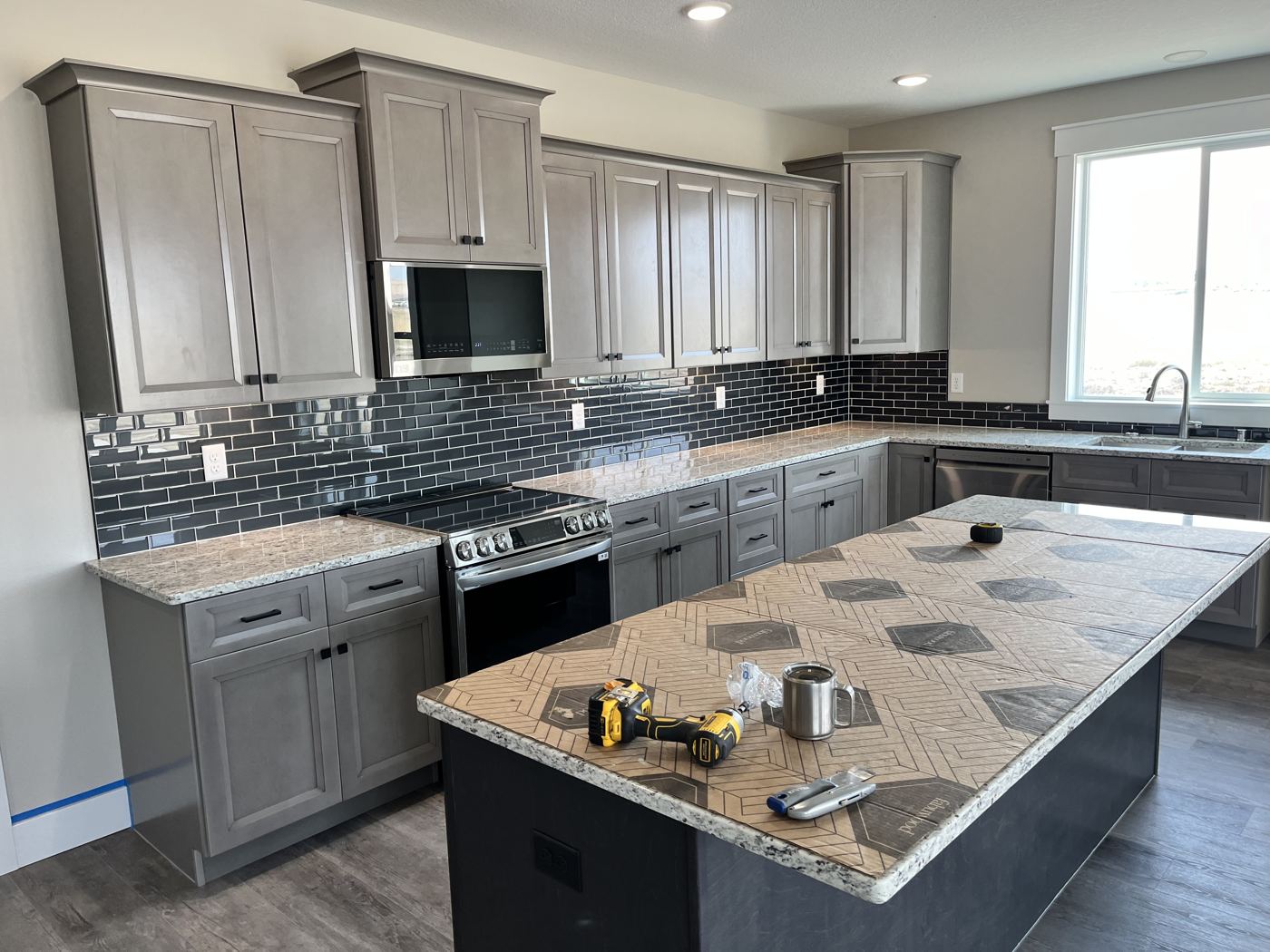 Gray kitchen near the finish with dark glass tile and a stone island top