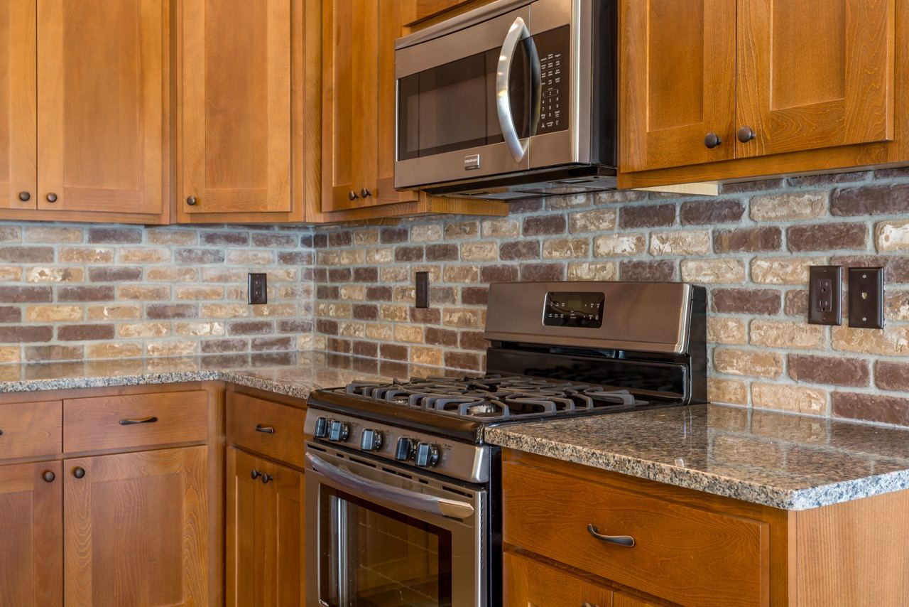 Stained cabinets, granite counters and brick backsplash around the range